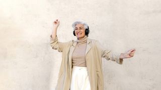 a woman dancing with headphones against a beige wall