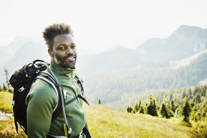 A fit, attractive middle-aged man poses while backpacking in the mountains.
