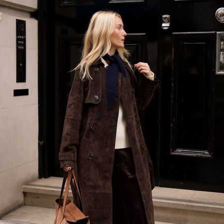 Chloe wears a brown sued trench coat, cream knit and brown trousers