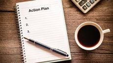 A notebook with the words Action Plan at the top sits on a wooden tabletop with a cup of coffee and a calculator.