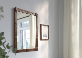 A white wall with a brown rattan framed mirror and photo frame
