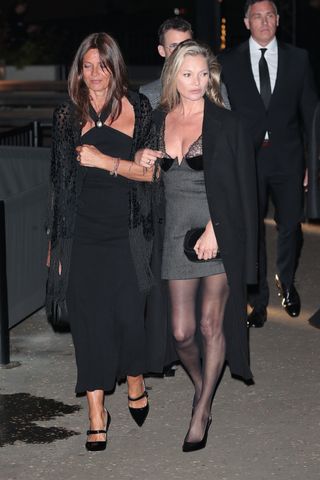 Kate Moss attending the Gucci show at the Tate Modern in London wearing a gray Gucci lingerie minidress and a black coat with tights and Gucci slingback heels.