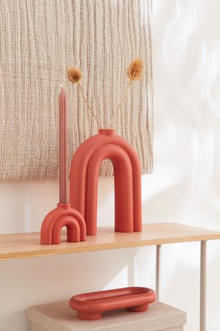 burnt orange rainbow-shaped candlestick on a table with a larger vase in a similar style