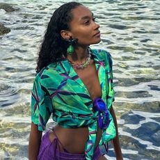 Photo of a woman wearing swim shorts, a printed top, and chunky sunglasses in the ocean