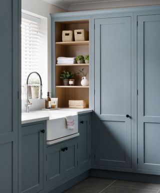 Blue laundry room with fitted cabinets and butler sink, with open shelving and neat built in shelves with baskets