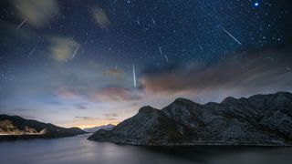 Geminid meteor shower occurring above a large lake surrounded by hills. The shooting stars streak across a star-studded sky. 