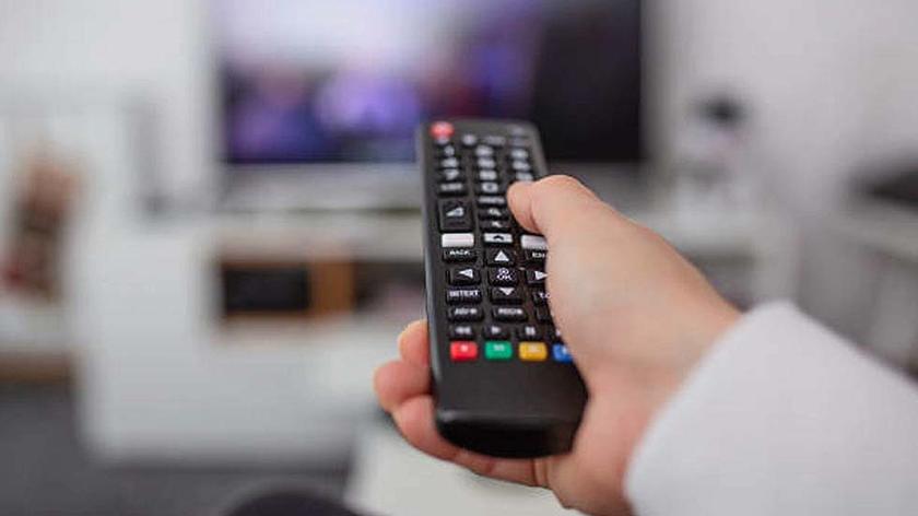 Watching TV and using remote controller. Hand with remote controller changing channels or opening apps on smart tv