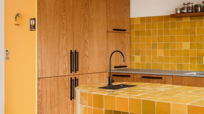 yellow kitchen with timber cabinetry, black handles, yellow zellige tile countertop and backsplash, with floating timber shelves and black tapware