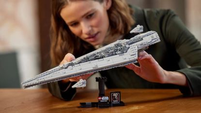 The Lego Executor Super Star Destroyer set on its stand on a wooden table, being posed by a woman