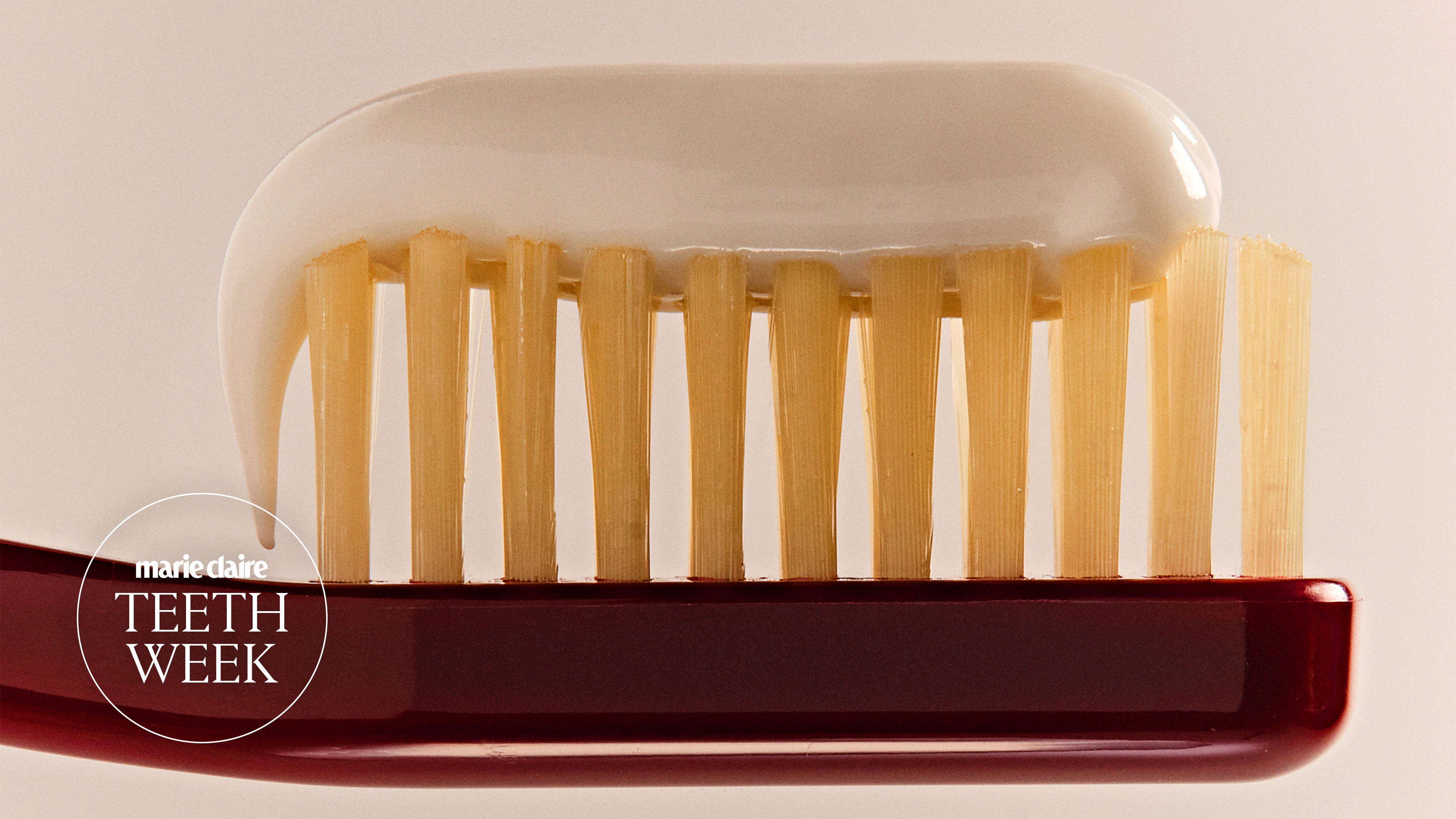 white toothpaste on burgundy toothbrush on a cream background