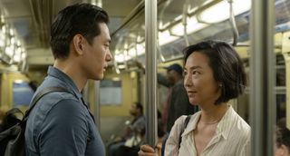 a couple (Teo Yoo as Hae-sung, Greta Lee as Nora) stand facing each other while holding on to a New York subway poll, in 'Past Lives' (2023)