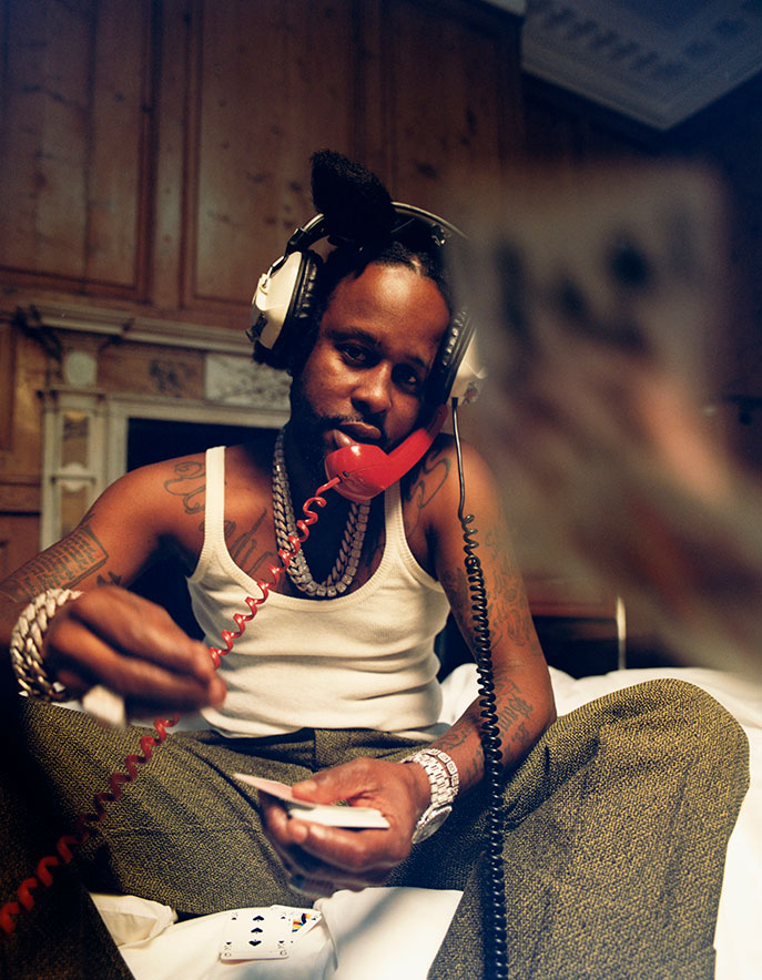 A DJ named Popcaan sits on a chair on the phone wearing headphones