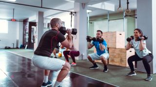 Group of people perform dumbbell front squat in gym