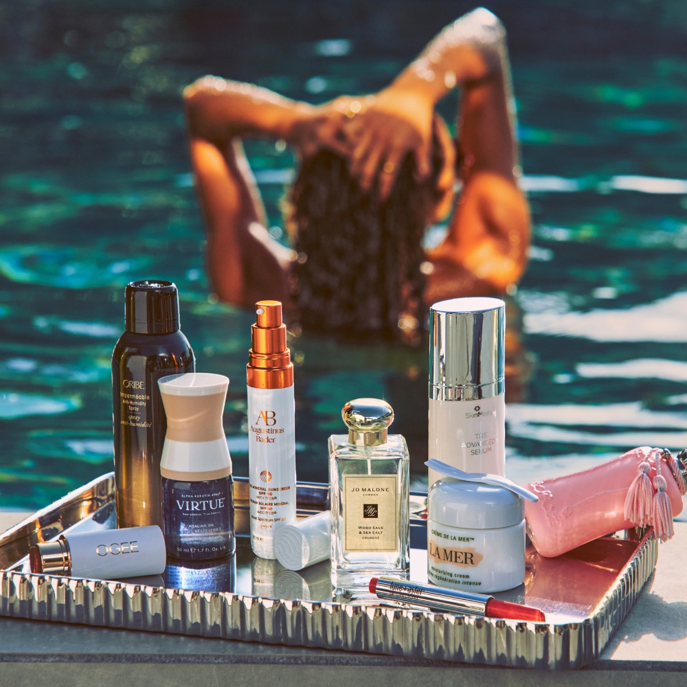 Woman facing away in the pool, in the front a silver tray with Bluemercury brands and products.