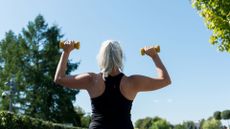 woman with dumbbells in shoulder press overhead looking at the sky