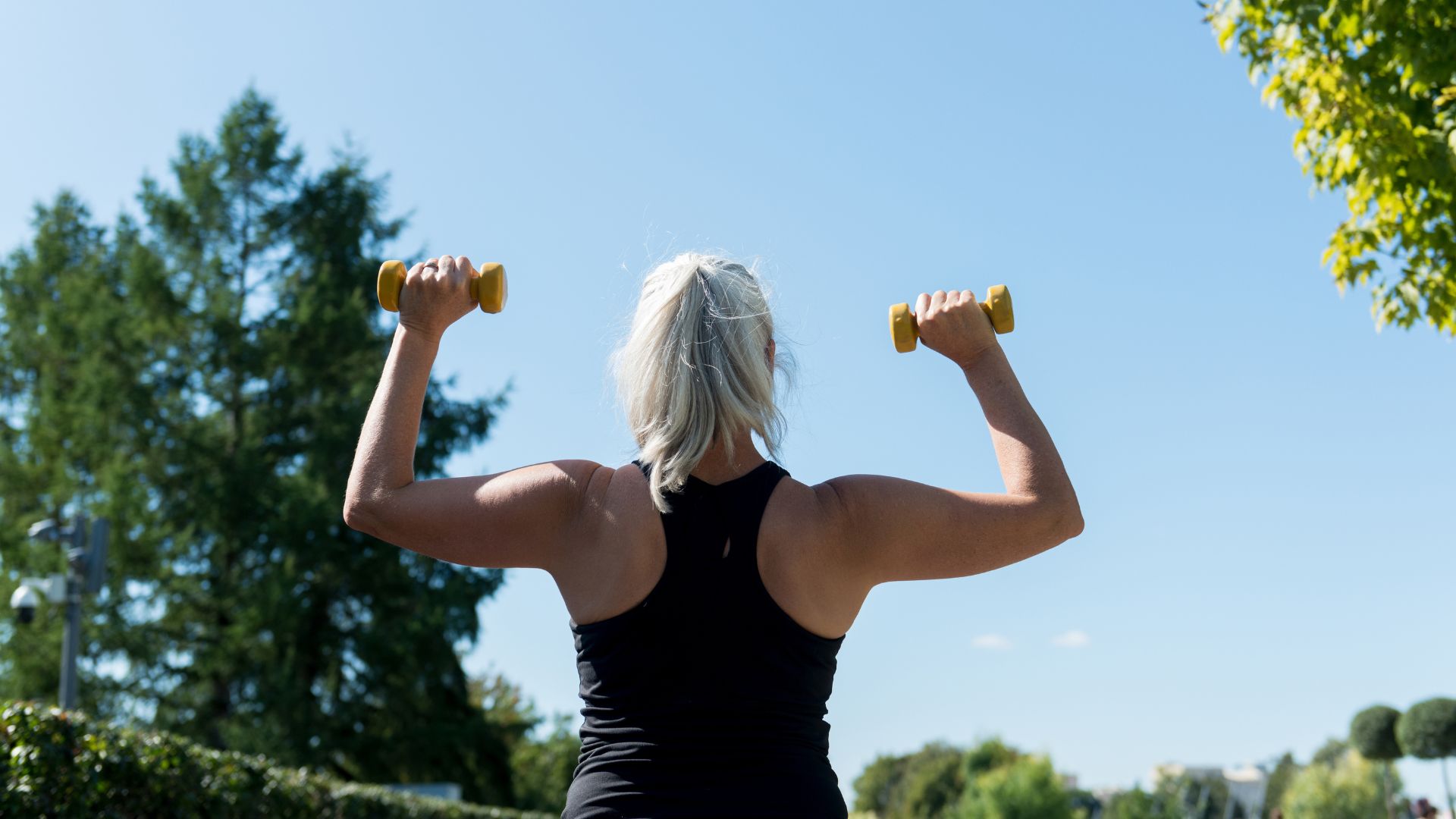 woman with dumbbells in shoulder press overhead looking at the sky