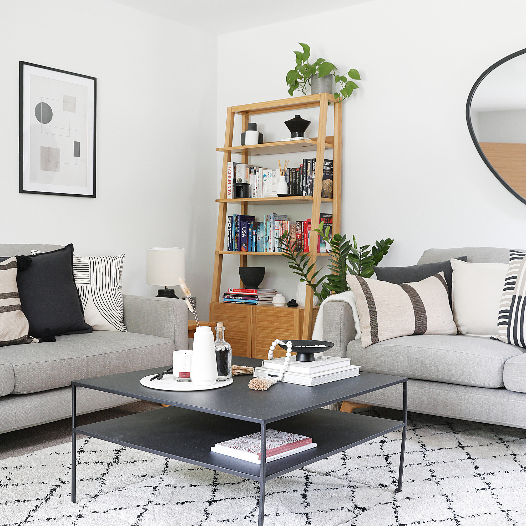white living room with two grey sofas and wooden ladder style shelving units with houseplants, a minimalist grey coffee table in centre and berber style rug on the floor