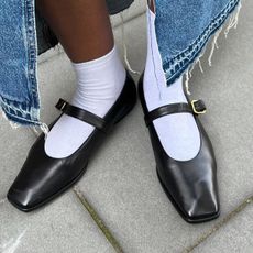 Woman wearing black Mary Jane flats with white sock and denim skirt.