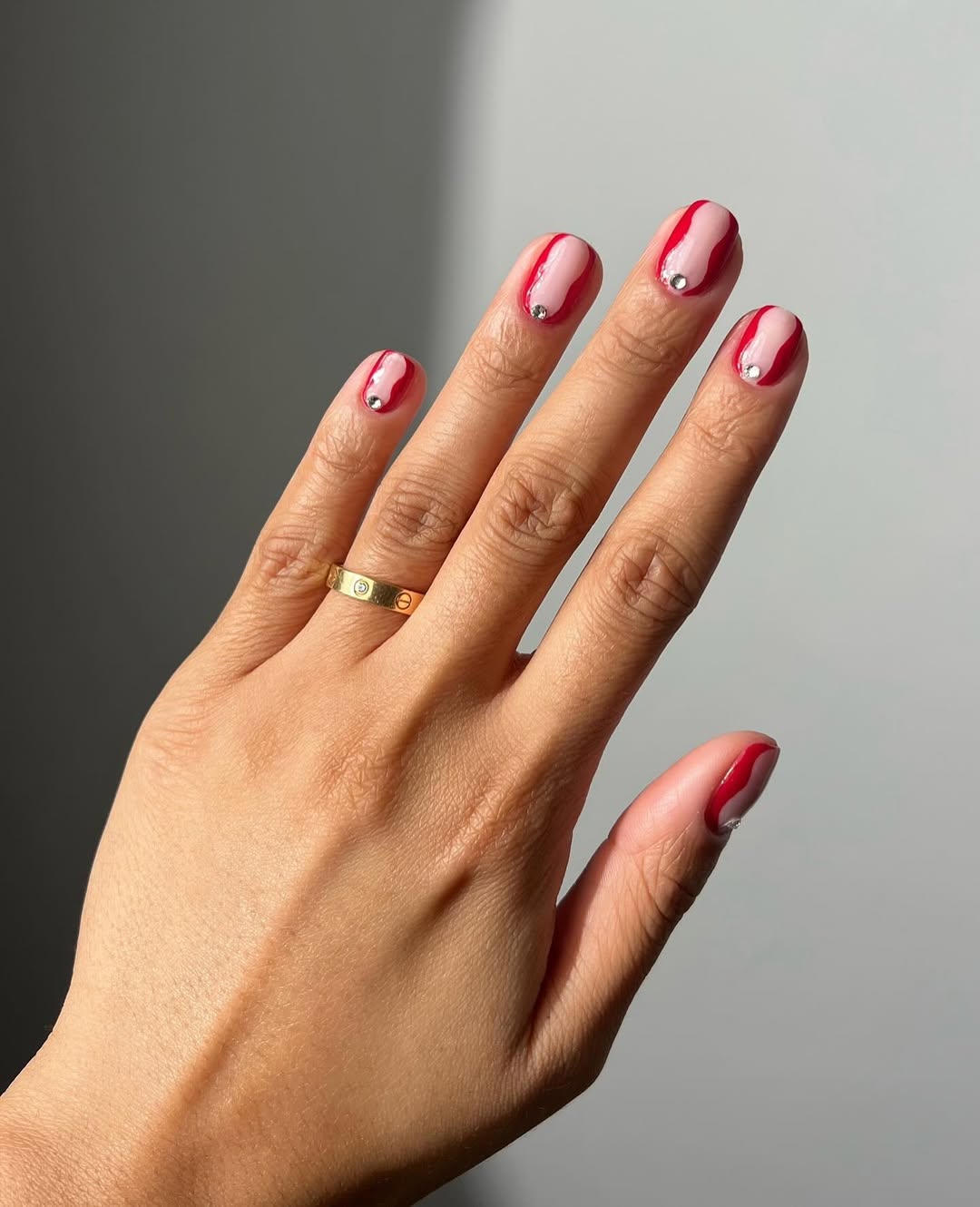A red, negative space manicure with gemstone details by Iram Shelton
