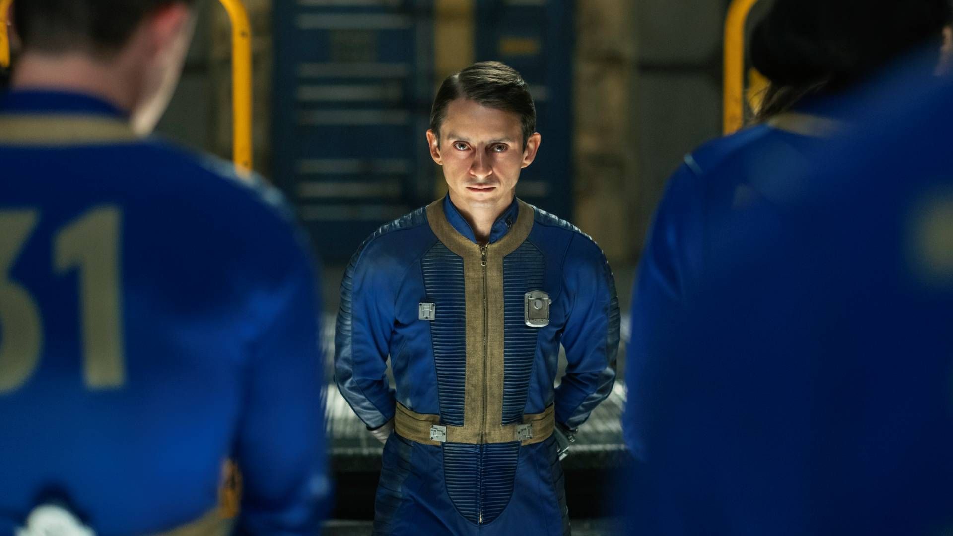 Moises Arias as Norm wearing a blue and yellow Vault suit in Fallout season 2