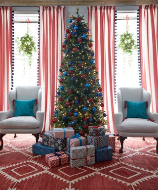 A decorated Christmas tree with an armchair either side and wrapped presents at the base. Red and white curtains by the French doors in the background.
