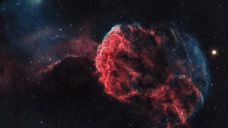 A vibrant nebula in space, with glowing red and blue filaments against a dark starry background