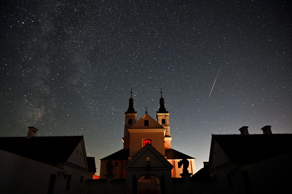 Dieses Langzeitbelichtungsfoto zeigt einen Meteor, der den Nachthimmel über einem großen Gebäude vor einem Sternenhimmel überquert.