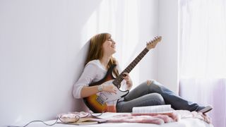 Girl plays a Strat-style guitar on a bed against a white wall