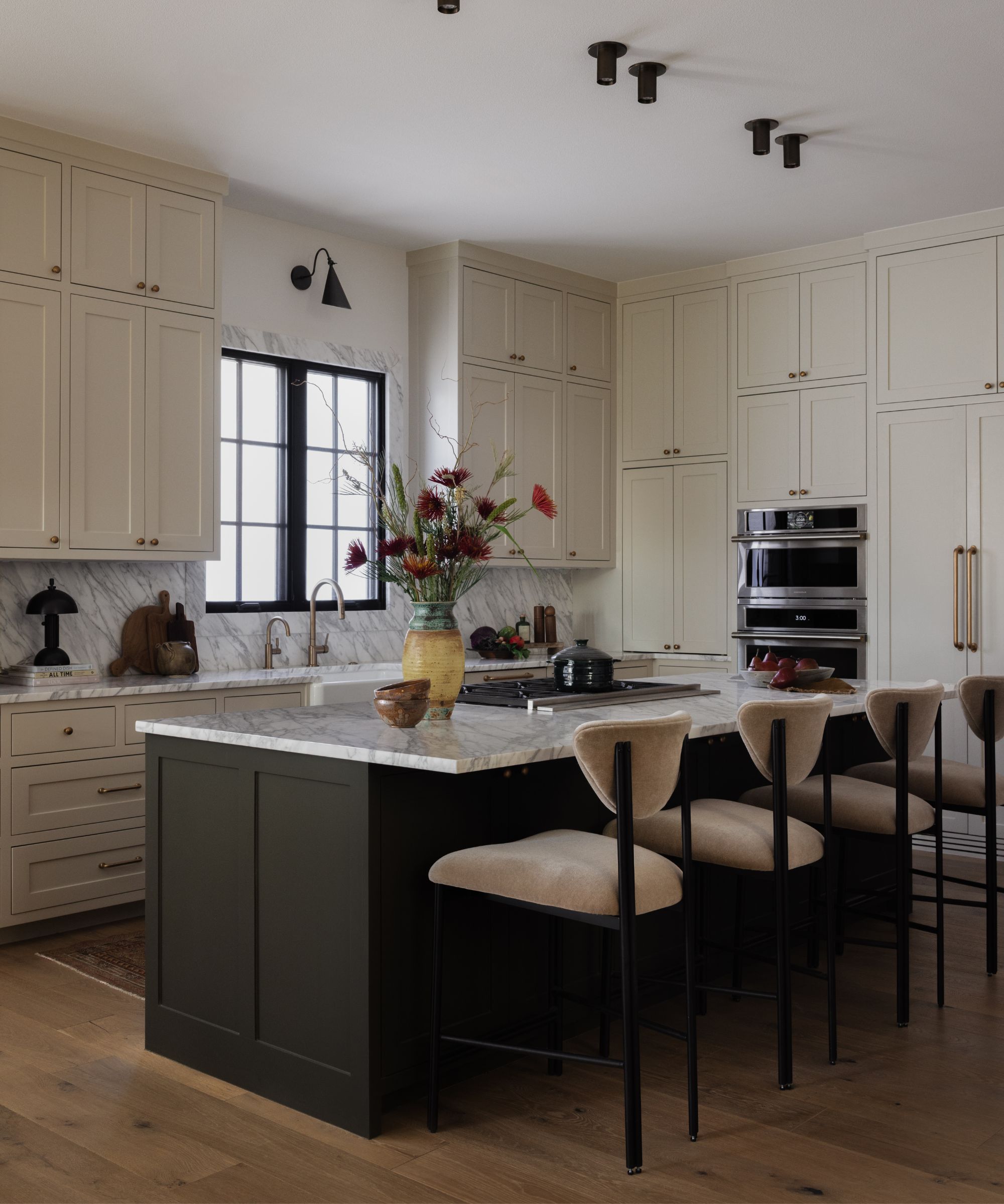 a warm neutral kitchen with cabinetry to the ceiling, marble countertops and a dark central kitchen island with bar stools