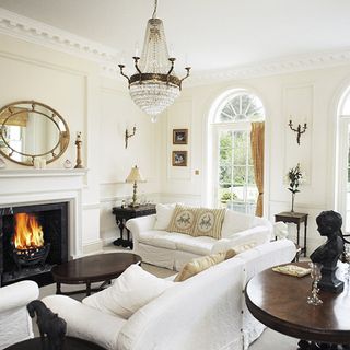 A white living room with white sofas, ornaments and statues on side tables and an open fire