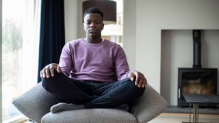 man meditating in a purple sweater in a living room