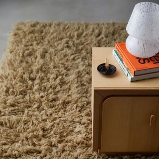 A Flokati Wool Shag Rug underneath a side table laid with books and a lamp