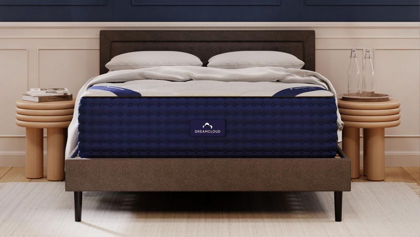 The image shows the DreamCloud Hybrid Mattress on a grey bed foundation in a neutrally decorated bedroom