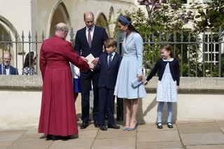 Britain's Prince George of Cambridge shakes hands with Dean of Windsor, The Right Revd David Conner (L) as he leaves with Britain's Prince William, Duke of Cambridge, Britain's Catherine, Duchess of Cambridge and Britain's Princess Charlotte of Cambridge (R) after attending the Easter Mattins Service at St. George's Chapel, Windsor Castle on April 17, 2022.