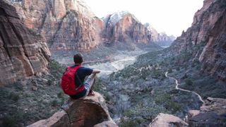 A hiker sits on a rock looking down at Zion Canyon in Utah