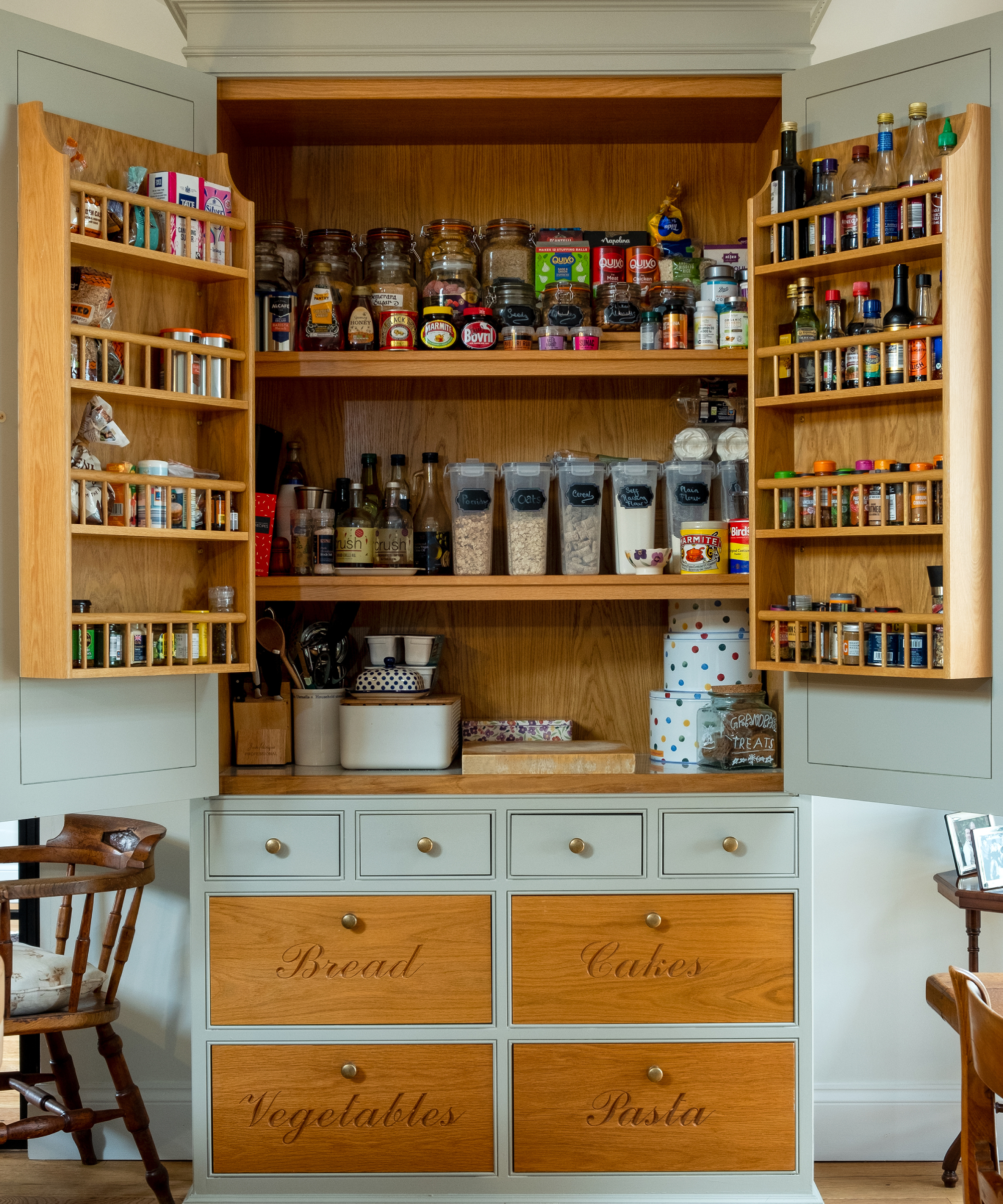 wooden and green pantry unit with shelving, drawers with words and racked shelving on inside of doors