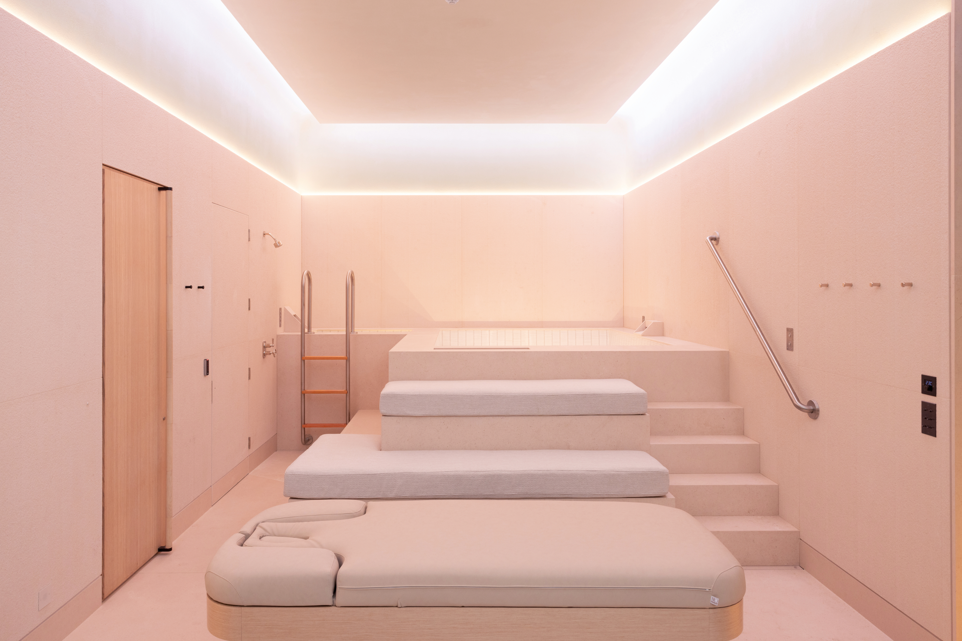 An onsen with warm white walls and steps with seat cushions leading up to the bathing area