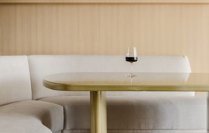 A dining table with a single wine glass kept atop. And a curving sofa surrounding it