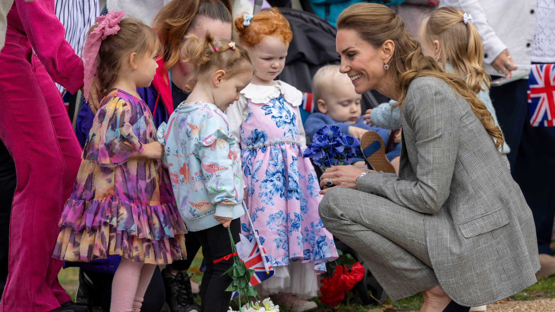 Kate Middleton kneeling down in a gray suit talking to little girls