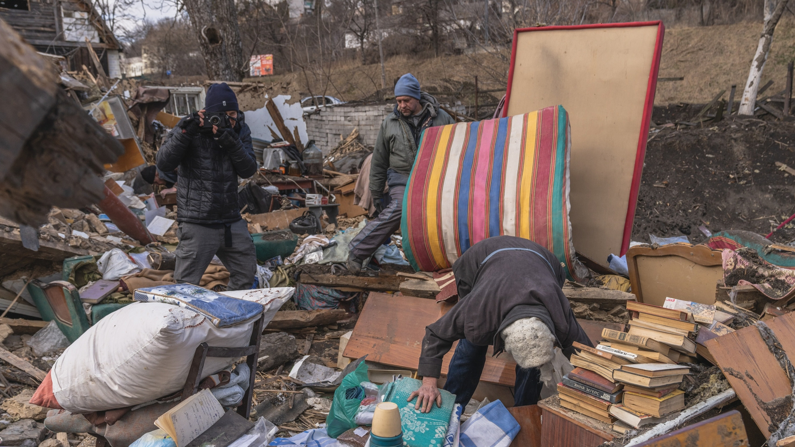 A photographer takes a picture of a man standing among rubble.