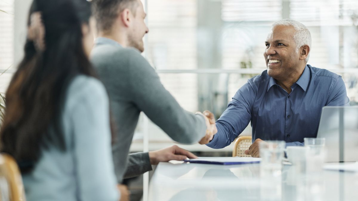 Two men shaking hands smiling while sitting at a table