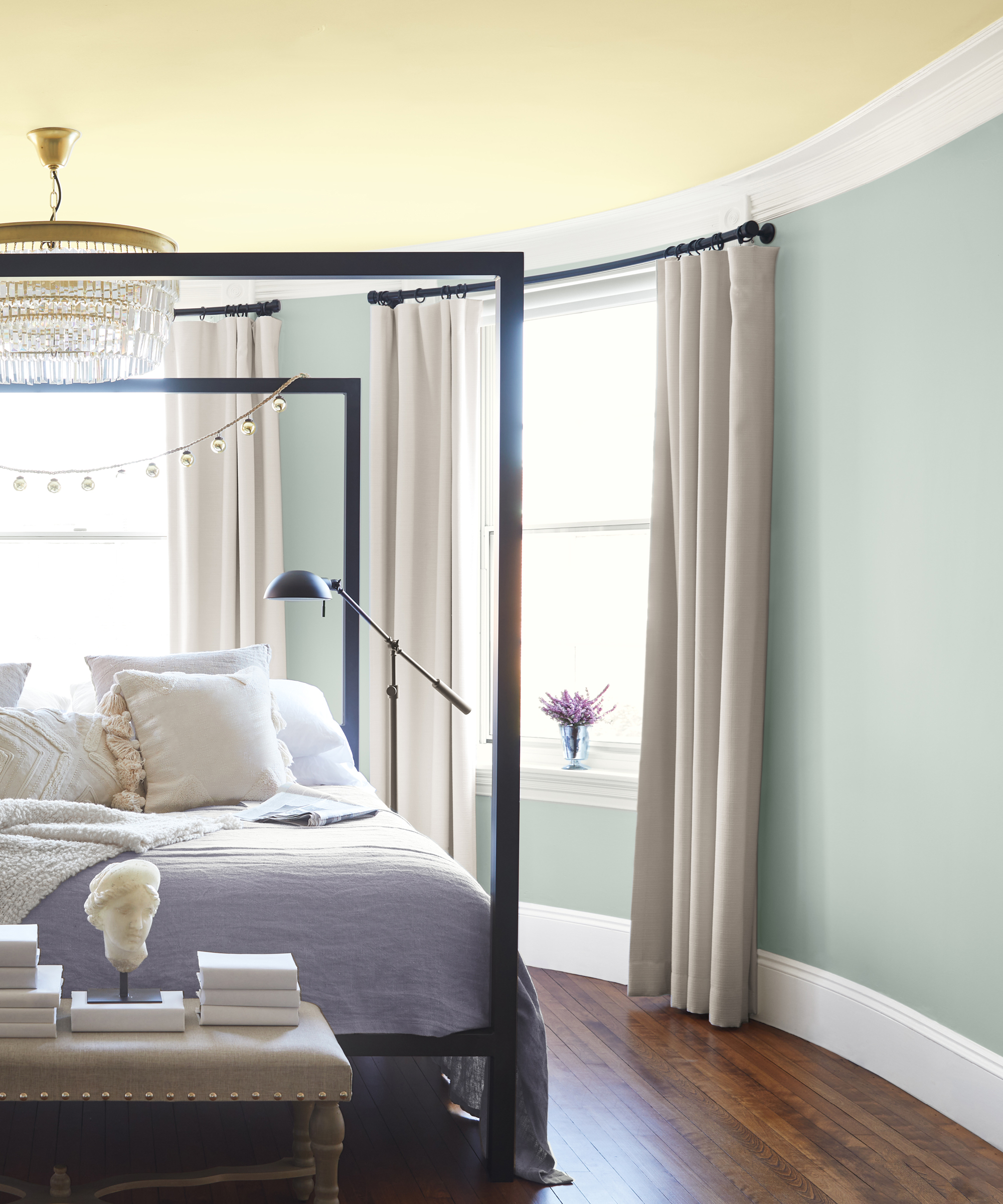 Yellow painted ceiling with light green walls, and black four-poster bed with crystal chandelier.