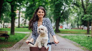 woman cycling in park with white dog in basket