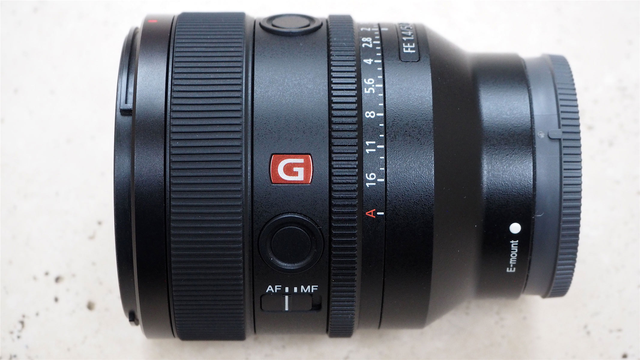 A side view of the Sony 50mm f/1.4 GM lens on a table, showing the red G logo.