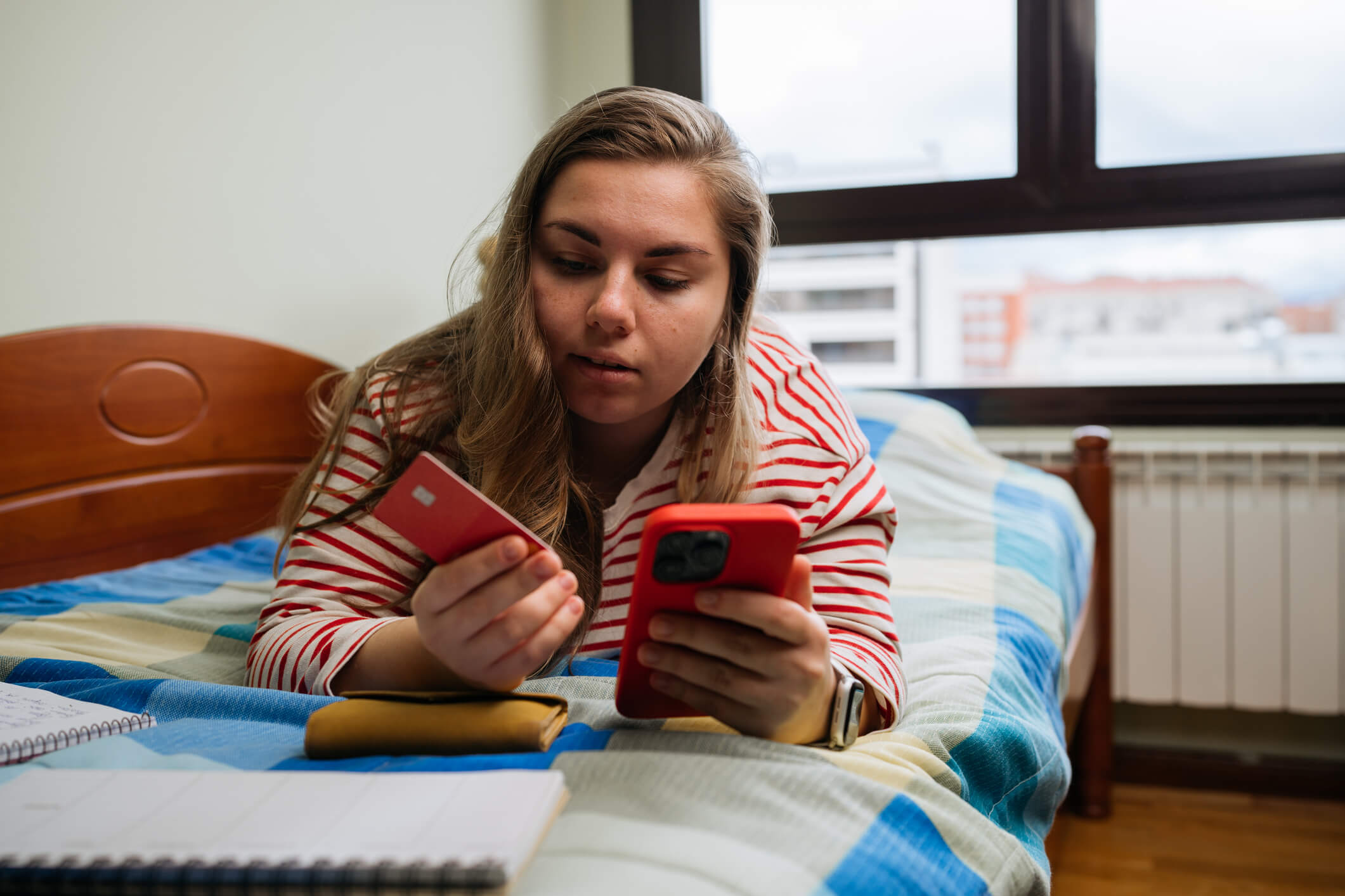 Young Woman with Credit Card and Smartphone on Bed Planning Expenses