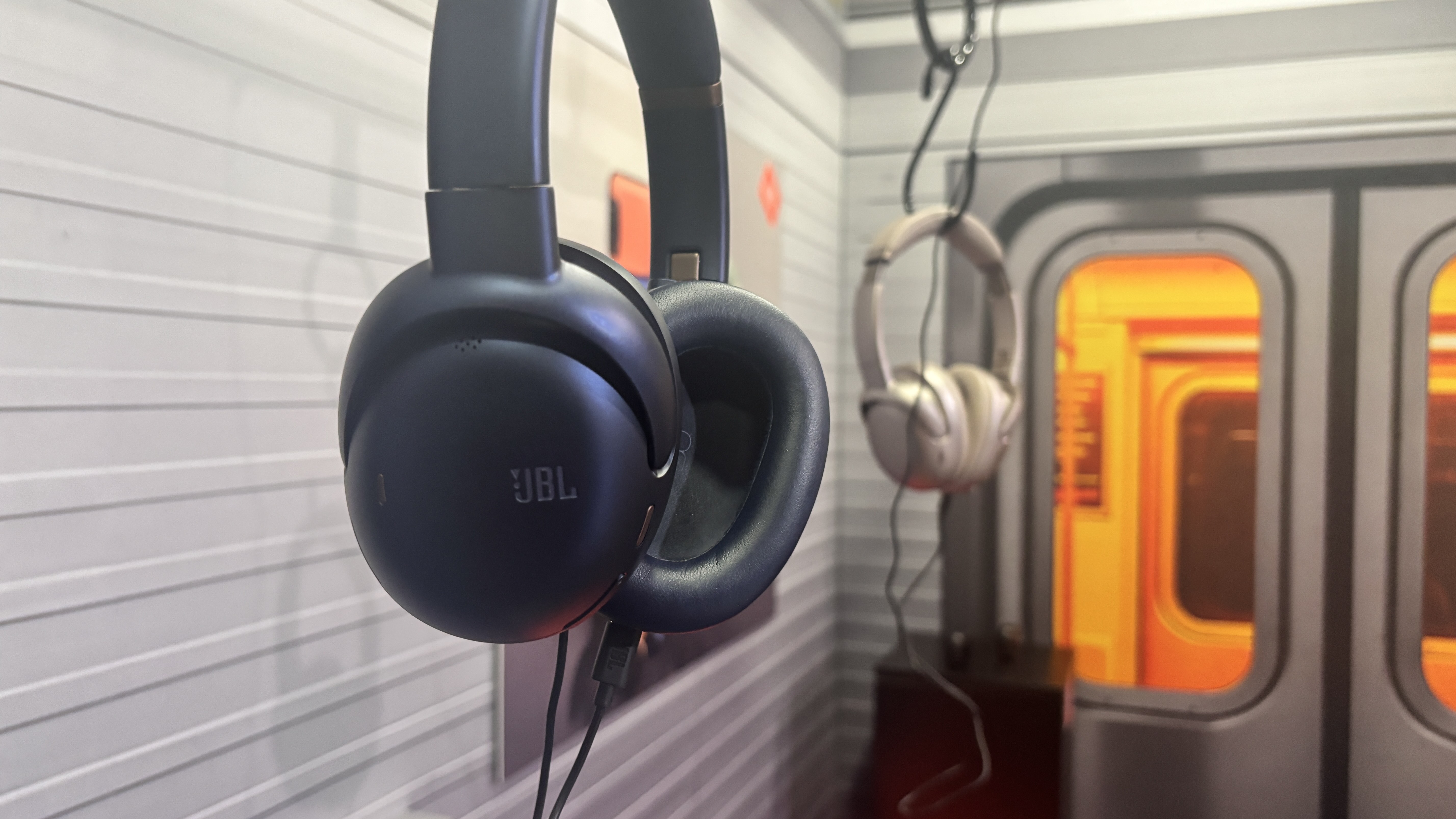 JBL wireless headphones hung from a mock subway carriage handle