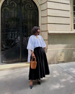 A influenciadora francesa Frann Fyne em roupa chique, com camisa branca, saia rodada preta e bolsa cesta.