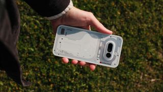 Hand holding the Nothing Phone (4a) horizontally outdoors, showing the transparent-inspired rear panel and camera module.