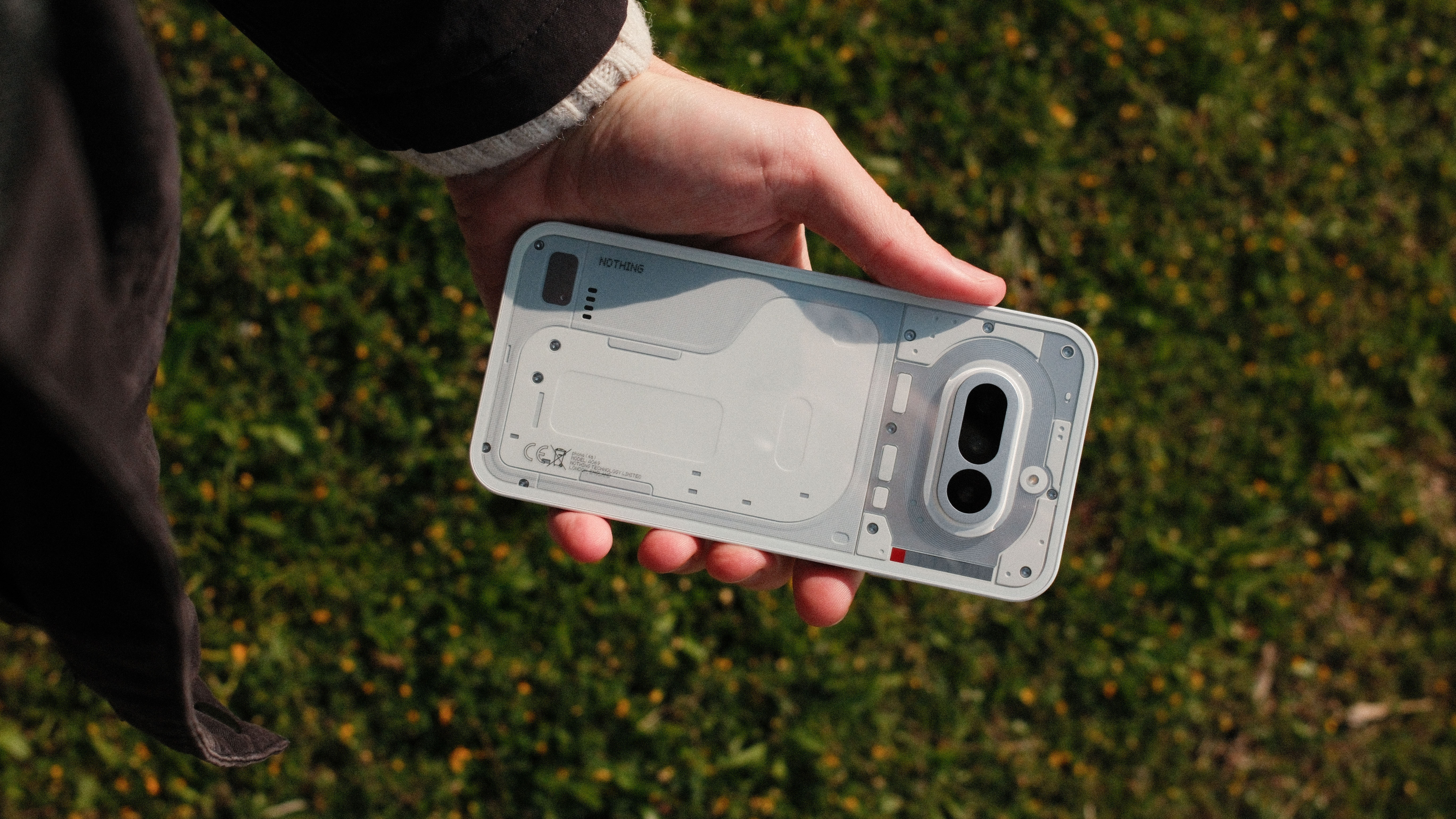 Hand holding the Nothing Phone (4a) horizontally outdoors, showing the transparent-inspired rear panel and camera module.