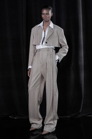 A female model wearing brown baggy pants and a matching short jacket with a white shirt under it.